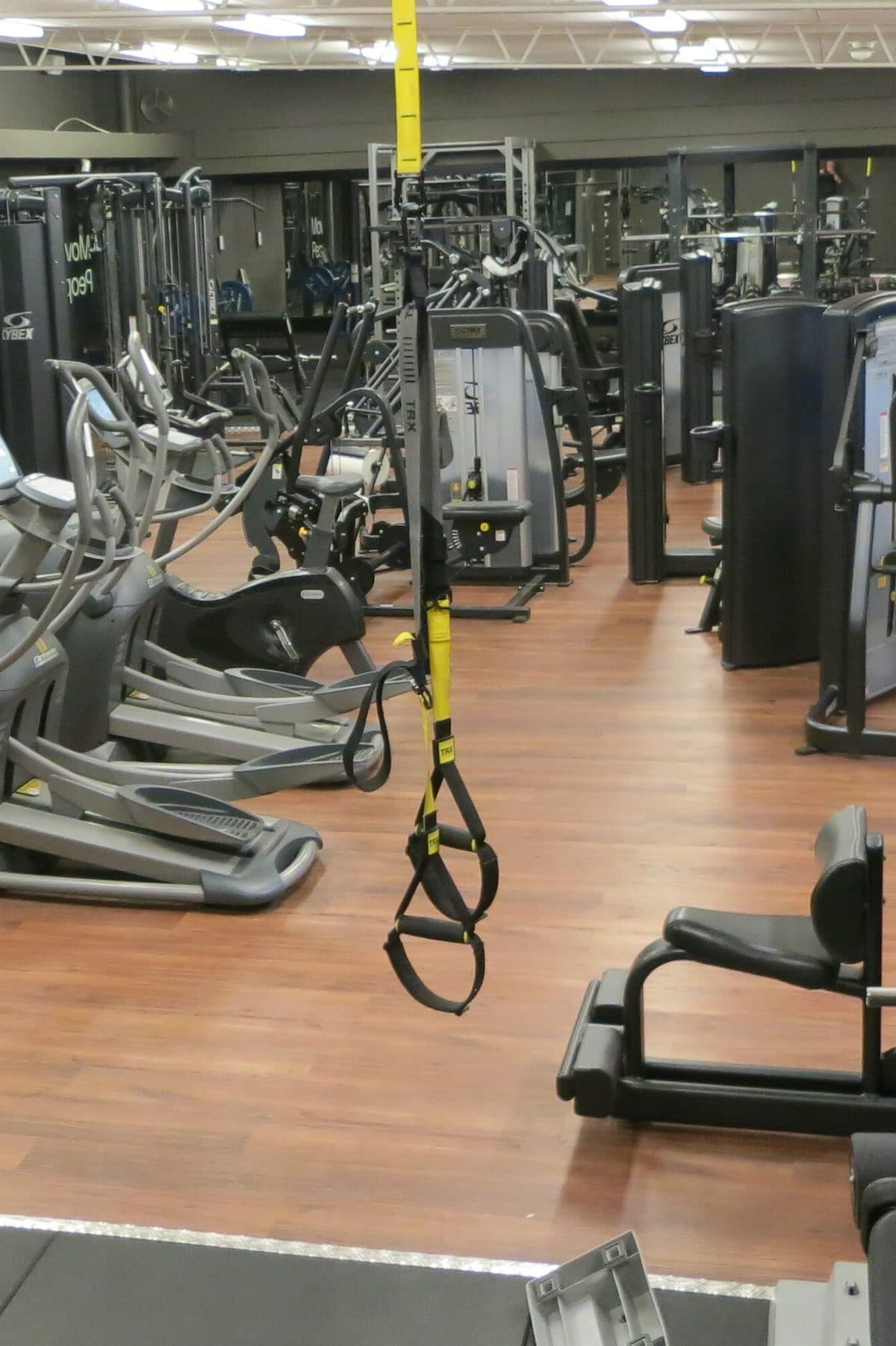 Sala de un gimnasio vacío, con cintas de correr, elípticos y correas de suspensión amarillas