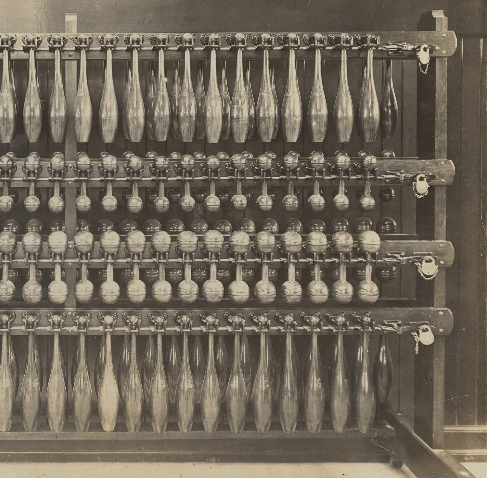 Fotografía de 1904 de un rack de mazas y mancuernas de madera, con un candado en cada fila